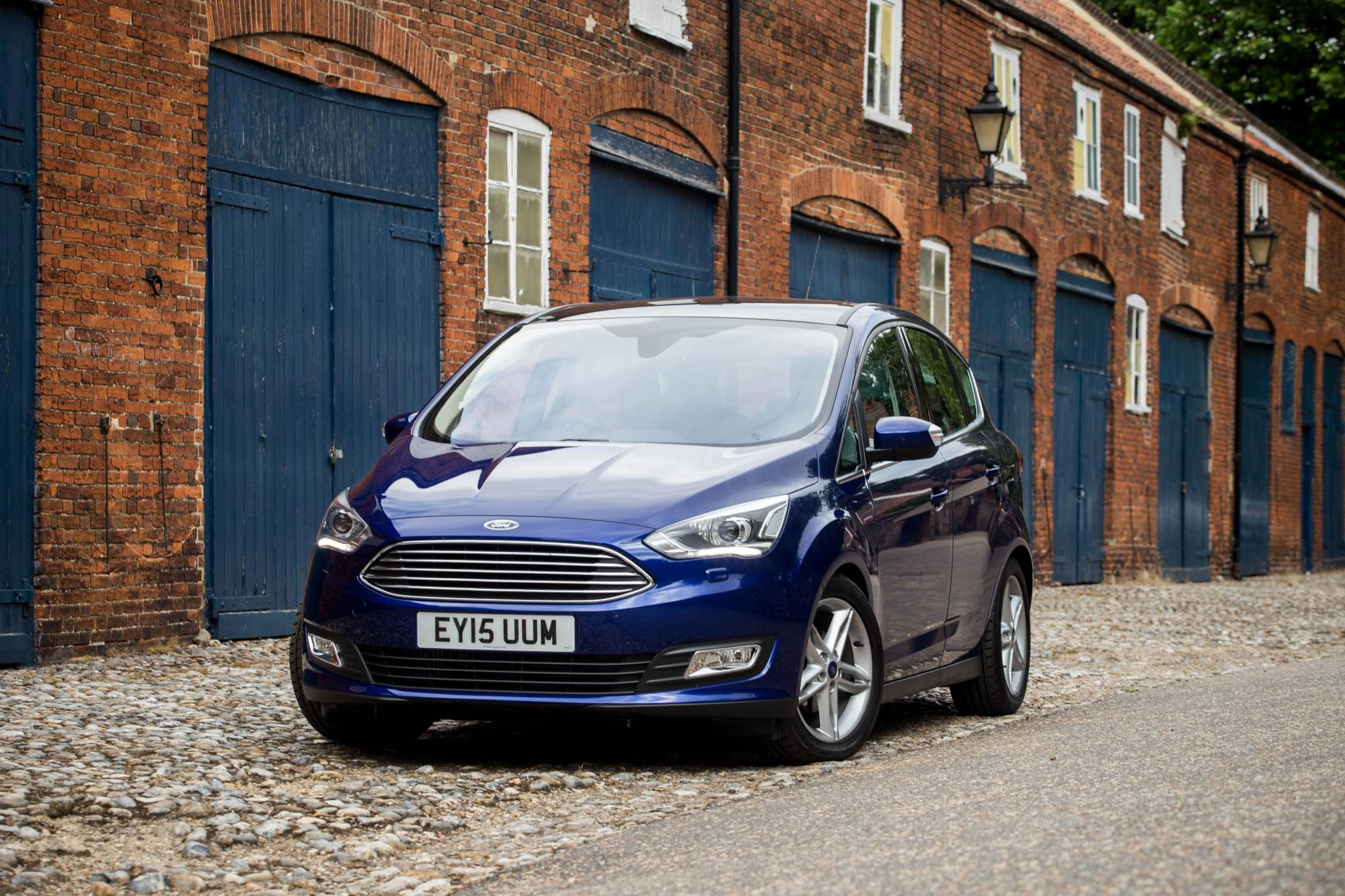 Blue Ford C-Max parked facing front on a cobbled street in front of a row of workshops